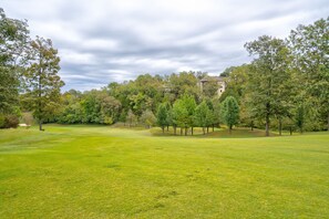 A golf course with a well-maintained green, trees, and a building in the background. - Golf Course View from Screened Porch, Near Silver Dollar City with Free Tickets, Gated Resort (Reeds Spring)