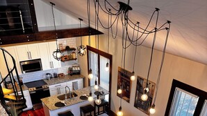 Cocina moderna con encimeras de granito, horno empotrado y comedor con sofá rojo y una mesa pequeña.
