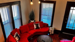 Una sala moderna con un sofá seccional rojo, una mesa de centro redonda y un sillón rojo. Hay varias bombillas colgantes y un ventilador de pie.