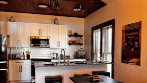 Una cocina moderna con armarios blancos, un refrigerador de acero inoxidable y un techo de madera.