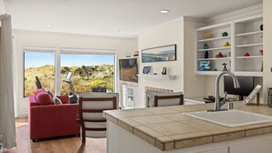 Een moderne keuken met een groot eiland, een zithoek met een rode bank, en uitzicht op de omgeving.