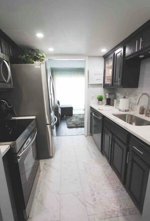 Una cocina moderna con electrodomésticos de acero inoxidable, armarios oscuros y piso de mármol.