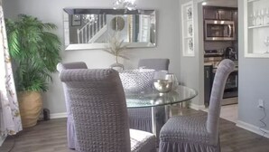Un comedor con una mesa de vidrio, sillas tapizadas en gris, un cuenco decorativo y una planta en maceta.