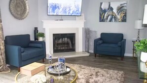 Una sala de estar con dos sofás azules, una chimenea, un televisor de pantalla plana y arte abstracto en la pared.