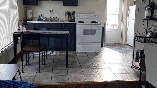 Une cuisine moderne avec des meubles de couleur sombre, une cuisinière blanche et un coin repas comprenant une table et des chaises.