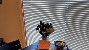 Une table à manger avec un set de table, un livre, un vase de fleurs et un bol de collations.