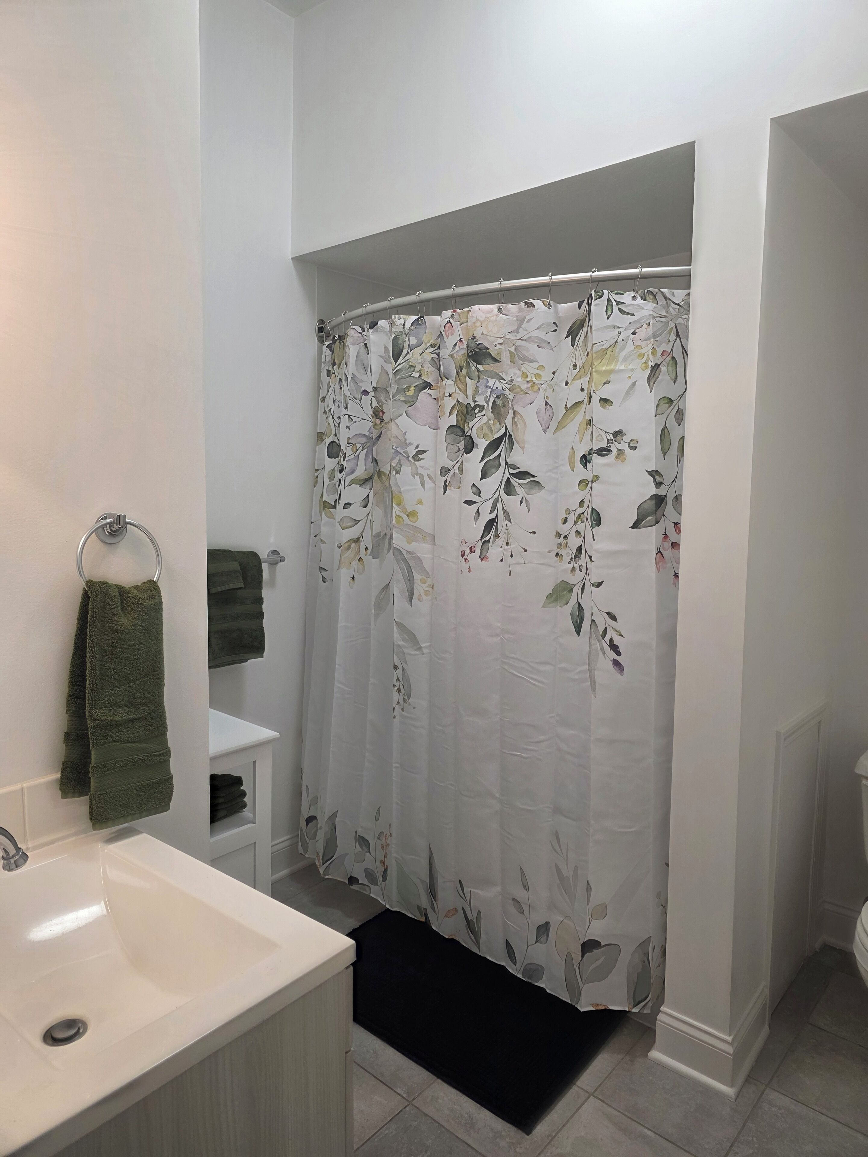 Un baño con un lavamanos blanco, una toalla verde y una cortina de ducha con estampado floral.