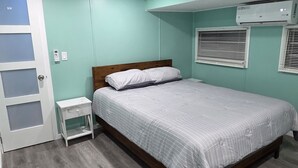 Een slaapkamer met een bed, nachtkastje, een deur met geëtste glaspanelen en een airconditioner aan de muur.