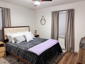 Une chambre à coucher avec un lit, des tables de chevet, un ventilateur de plafond et une fenêtre avec des rideaux.