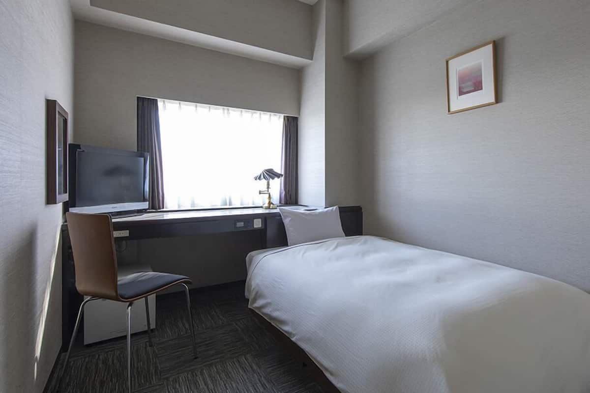Une chambre d’hôtel avec un lit, un bureau, une chaise, une télévision et une fenêtre avec des rideaux.