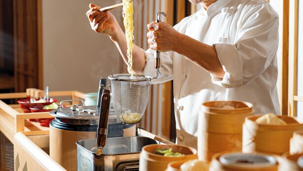 Un chef prepara fideos con un colador y utensilios de cocina.