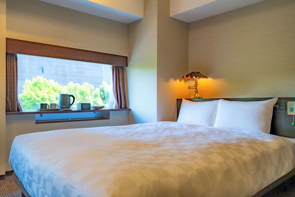 A hotel room with a large bed, a window with curtains, a bedside table with a lamp, and a view of greenery outside. - Koraku Garden Hotel (Tokyo)