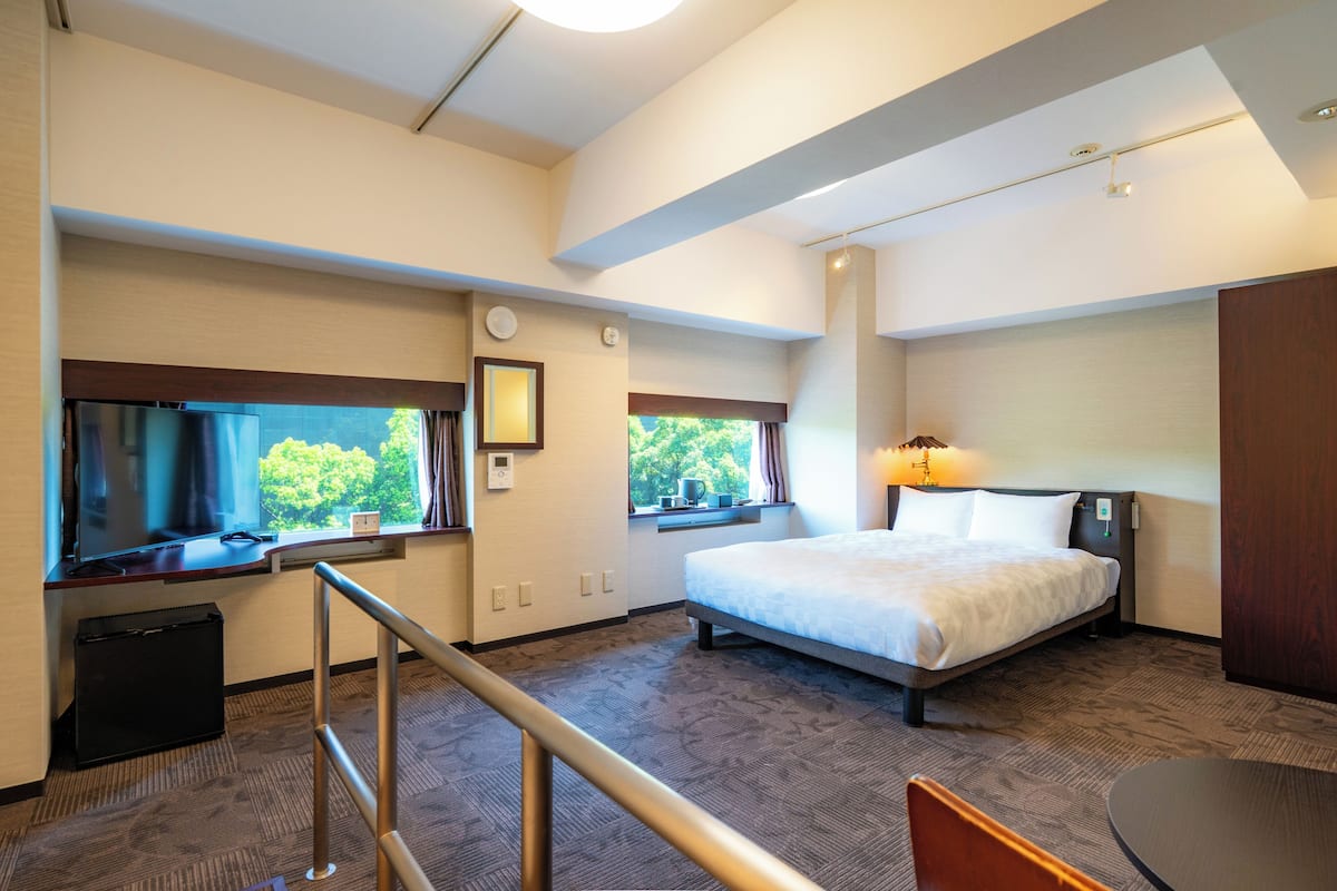 Une chambre d’hôtel avec un lit, un bureau avec un ordinateur, une fenêtre donnant sur un paysage agréable et une petite table.