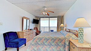 Une chambre à coucher comprenant un lit, une chaise, une commode, un téléviseur et un ventilateur de plafond.
