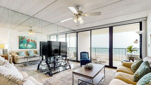 Un salon spacieux doté d’un grand téléviseur à écran plat, de sièges confortables, d’un ventilateur de plafond et d’un balcon avec vue.