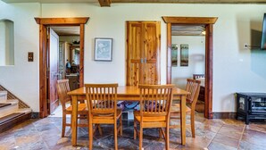 Un comedor con una mesa y sillas de madera, piso de baldosas y una escalera que conduce a otra habitación.