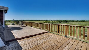 Una terraza de madera con barandilla, una mesa y sillas, con vistas a un campo cubierto de césped.