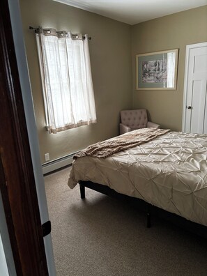 Une chambre à coucher avec un lit, une chaise, une porte et une fenêtre avec des rideaux.