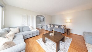 A modern living room with a sectional sofa, a coffee table, and a lamp. - 3BR/2BA Home – 30 Mins to YVR, Family-Friendly (Delta)
