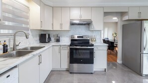 A modern kitchen with white cabinets, stainless steel appliances, and a marble backsplash. - 3BR/2BA Home – 30 Mins to YVR, Family-Friendly (Delta)