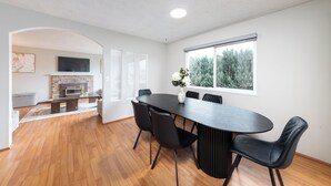 A modern dining area with a dark wooden table and black chairs, a fireplace, and a large window with a view of trees. - 3BR/2BA Home – 30 Mins to YVR, Family-Friendly (Delta)