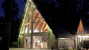 Una casa moderna con un amplio ventanal de vidrio y un techo inclinado, rodeada de árboles.