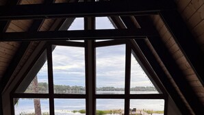 Una habitación acogedora con un ventanal grande que da a un lago, techo de madera y un sofá con cojines.