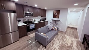 A modern kitchen with stainless steel appliances, a grey sofa, and a patterned rug.