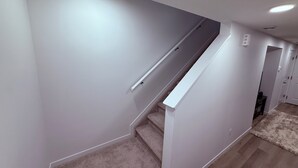 A modern interior with a staircase, carpeted stairs, and a hallway leading to a door.