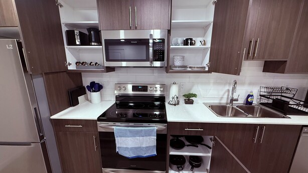A modern kitchen with stainless steel appliances, wooden cabinets, and a white countertop.