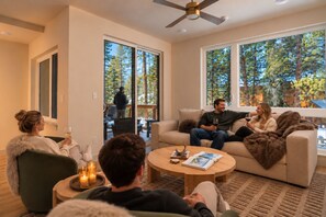 A modern living room with a sofa, coffee table, and a large window with a view of trees. - Luxe 3Br Townhome w/ Private Hot Tub, Sauna, Walk to Village and Gondola! (Dillon)