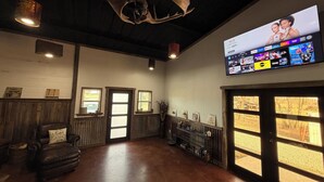 Una habitación amplia con una pantalla grande mostrando una película, un sillón de cuero, paredes de madera y un techo rústico.