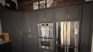Una cocina con armarios grises oscuros, horno de acero inoxidable y refrigerador.