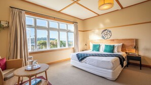 A hotel room with a large bed, a small table with glasses, a chair, and a view of the outdoors. - Lake Brunner Eco Lodge (Inchbonnie)