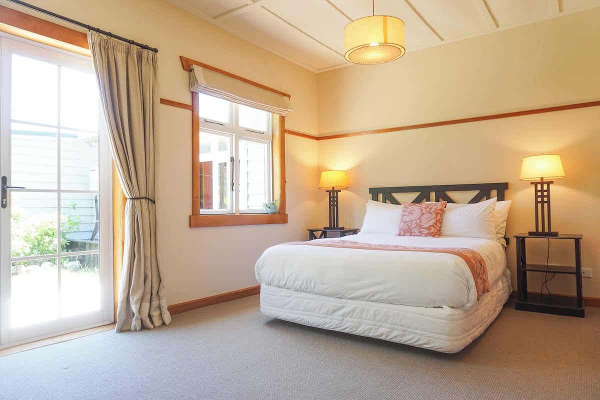 A bedroom with a large bed, two bedside tables with lamps, a window with curtains, and a ceiling light fixture.