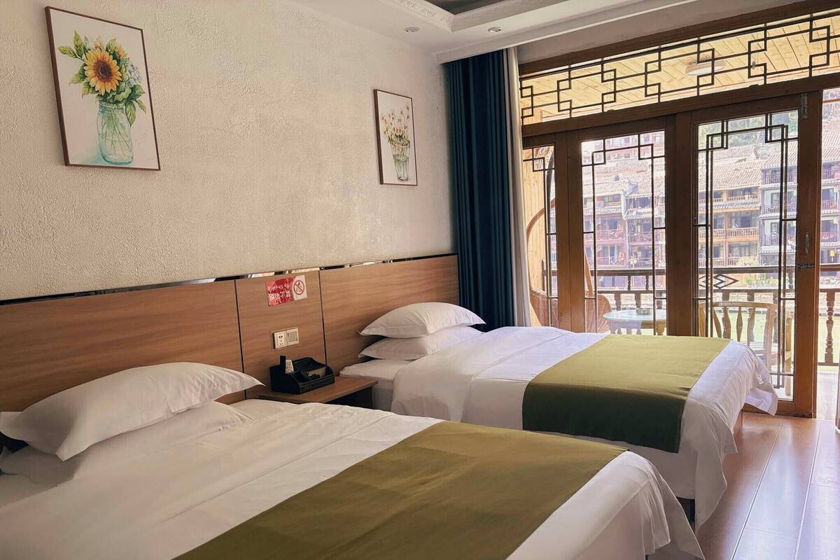 A hotel room with two beds, a nightstand, and a window with a view of traditional buildings.