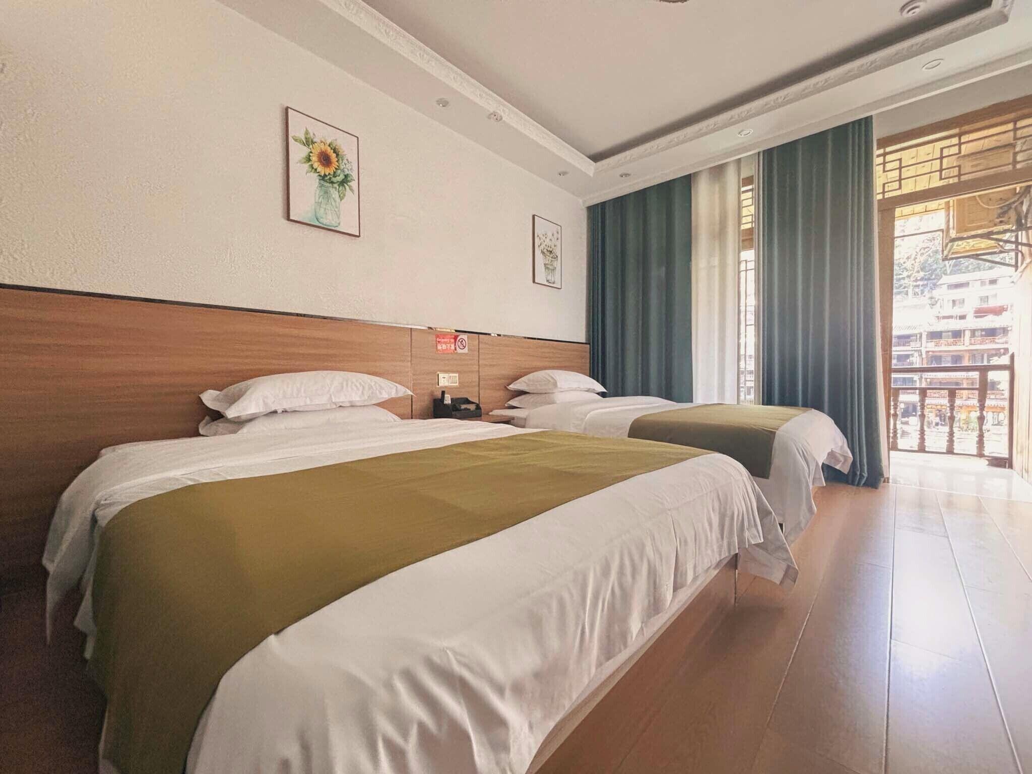 A hotel room with two beds, a wooden headboard, a large window with curtains, and a view of a building outside.