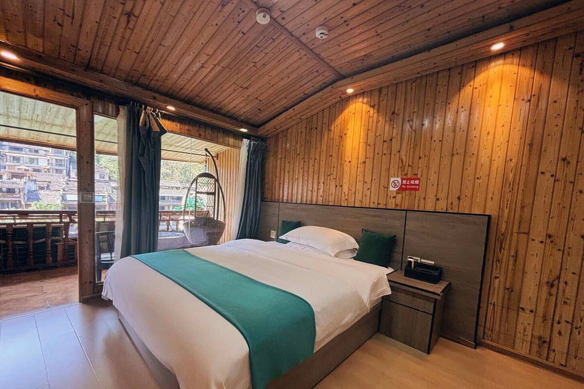 A wooden-paneled bedroom with a bed, a nightstand, and a hanging chair by the window.