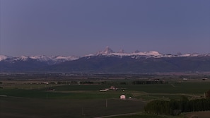 A rural landscape with a mountain range in the background and a small building in the foreground.