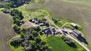 An aerial view of a rural property with a large field, a winding path, several RVs, and a few buildings.