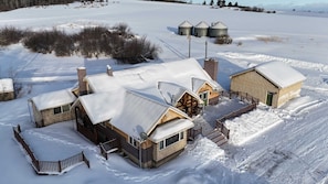A snow-covered farm with several buildings, including a main house with a large porch and a smaller shed.