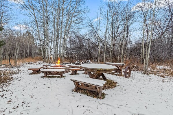 A snow-covered outdoor area with a fire pit and picnic tables.
