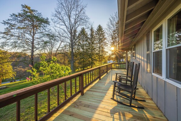 A wooden deck with a railing, a rocking chair, and a view of trees and a lake.