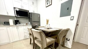 Een compacte keuken met witte kastjes, een magnetron, een koelkast en een eettafel met vier stoelen.