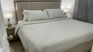 Een net opgemaakt bed met een beige hoofdeinde en witte beddengoed in een hotelkamer.