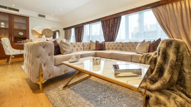 A modern living room with a sectional sofa, a glass coffee table, and a large window with curtains. - Marble Arch Residences (London)