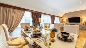 A dining area with a long table set for a meal, a sofa, and a TV mounted on the wall. - Marble Arch Residences (London)