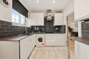 A modern kitchen with white cabinets, a built-in washing machine, and a black tiled backsplash. - Marble Arch Residences (London)