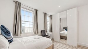 A bedroom with a bed, a wardrobe, a chair, and a window. - Marble Arch Residences (London)