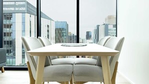 Un espace de salle à manger moderne avec une table rectangulaire et quatre chaises, de grandes fenêtres offrant une vue sur le paysage urbain.